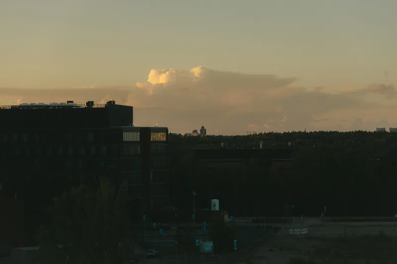Otaniemi at dusk: a dark office block against a sunset sky, forest and a few parked cars below